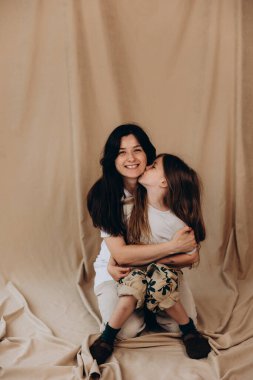 Bir fotoğraf stüdyosunda bej kumaş arka planına karşı poz veren genç anne ve kız.