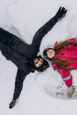 Mutlu baba ve kız karda oynuyor, kardan melekler yapıyor ve karda yuvarlanıyor.