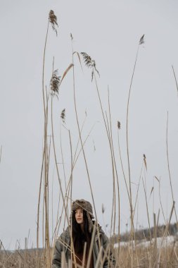 Sıcak, şık bir kış ceketi ve donmuş bir gölün arka planında kürk şapkalı, fotoğraf için poz veren ve karlı havanın tadını çıkaran bir kadının fotoğrafı.
