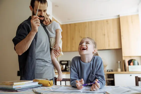 stock image a father checking his 6-year-old daughter's homework, a girl sitting at the kitchen table doing her homework in front of her father who is cooking in the kitchen