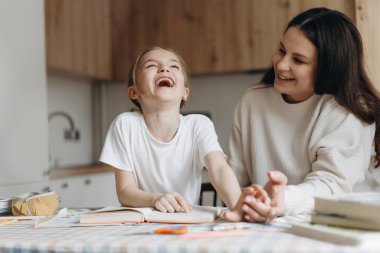 Genç bir anne ve mutlu bir kız. Etrafı kitaplarla ve kırtasiyelerle çevrili ahşap bir masada birlikte okuyorlar..