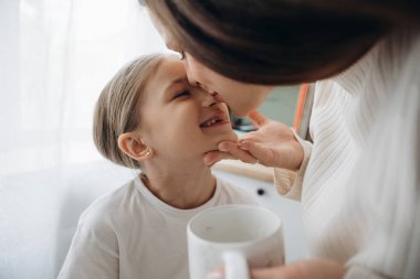 Bir anne ile mutlu küçük kızı arasında hassas bir an. Anne gülümseyen çocuğunu yanağından öpüyor..