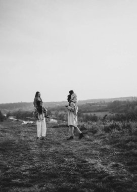 Nehrin kenarında duran şık, klasik bir aile, bir çocuk tutuyor, sakin, doğal bir ortamda, siyah-beyaz yakalanmış.