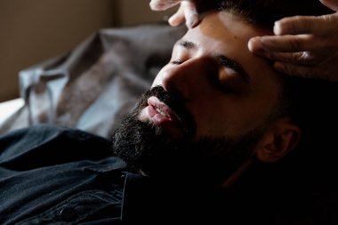 Şık sakallı adam güzellik salonunda yüz masajı yaptırıyor.