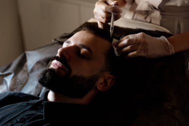 Çekici bir adam klinikte saç dökülmesini tedavi etmek için mezoterapi iğnesi olur. Deriye ve kafa derisine enjeksiyon.