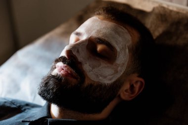 Güzellik, çamur ve nemlendirici maske için kaplıcada sakallı bir adamla yüz bakımı, cilt bakımı ve rahatlama. Sakinlik, masaj ve güzellik salonu için yüzüne sürtünen bir erkek ve kadın güzellik ürünüyle sağlık, terapi ve sağlık.