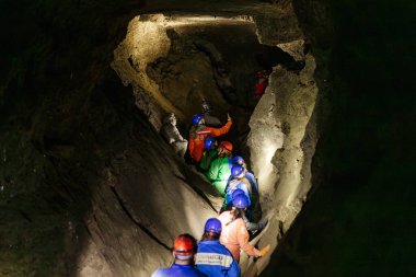 09.11.24 Mlynky, Ukraine: a photo from behind of people dressed in protective suits and helmets walking one after another inside a dark cave  clipart