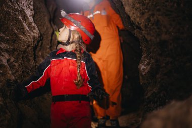Koruyucu takım elbiseli ve kasklı, elinde el feneri olan 6 yaşındaki bir kız mağaranın ortasında turistik bir yolda yürüyor. 