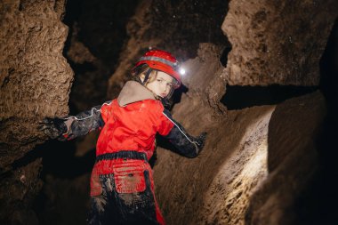 Koruyucu takım elbiseli ve kasklı, elinde el feneri olan 6 yaşındaki bir kız mağaranın ortasında turistik bir yolda yürüyor. 