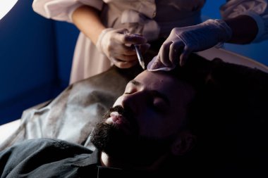 Çekici bir adam klinikte saç dökülmesini tedavi etmek için mezoterapi iğnesi olur. Deriye ve kafa derisine enjeksiyon.