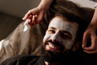 Güzellik, çamur ve nemlendirici maske için kaplıcada sakallı bir adamla yüz bakımı, cilt bakımı ve rahatlama. Sakinlik, masaj ve güzellik salonu için yüzüne sürtünen bir erkek ve kadın güzellik ürünüyle sağlık, terapi ve sağlık.