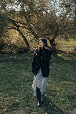 Çok doğal ve zarif bir kadın, doğanın arka planına karşı bir fotoğraf için poz verir, kadınlığını vurgulayan şık kıyafetler giyer.