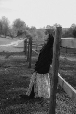 Çok doğal ve zarif bir kadın, doğanın arka planına karşı bir fotoğraf için poz verir, kadınlığını vurgulayan şık kıyafetler giyer.