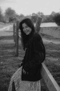 Çok doğal ve zarif bir kadın, doğanın arka planına karşı bir fotoğraf için poz verir, kadınlığını vurgulayan şık kıyafetler giyer.