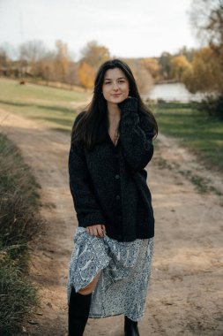 Çok doğal ve zarif bir kadın, doğanın arka planına karşı bir fotoğraf için poz verir, kadınlığını vurgulayan şık kıyafetler giyer.