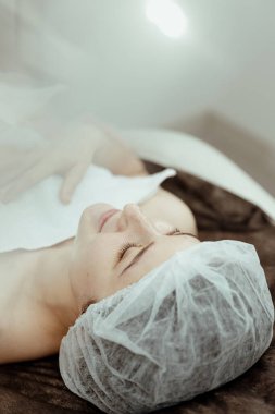 Bir kozmetik uzmanı genç bir kadının kafasında ve yüzünde güzellik prosedürü uygular..