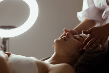 Bir kozmetik uzmanı genç bir kadının kafasında ve yüzünde güzellik prosedürü uygular..