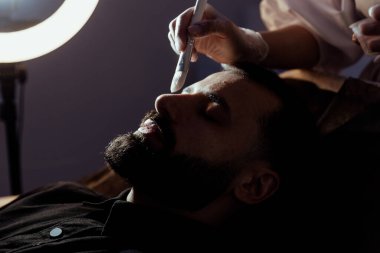 Güzellik uzmanında çeşitli güzellik tedavileri gören rahat genç bir adam sakallı bir adamın portresi güzellik iğneleri ve yüz maskeleri olan bir adam.