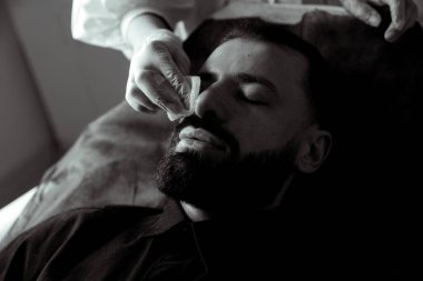 Güzellik uzmanında çeşitli güzellik tedavileri gören rahat genç bir adam sakallı bir adamın portresi güzellik iğneleri ve yüz maskeleri olan bir adam.