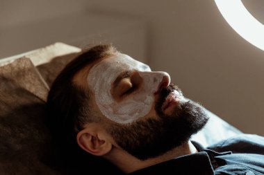 Güzellik uzmanında çeşitli güzellik tedavileri gören rahat genç bir adam sakallı bir adamın portresi güzellik iğneleri ve yüz maskeleri olan bir adam.
