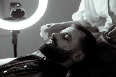 Güzellik uzmanında çeşitli güzellik tedavileri gören rahat genç bir adam sakallı bir adamın portresi güzellik iğneleri ve yüz maskeleri olan bir adam.