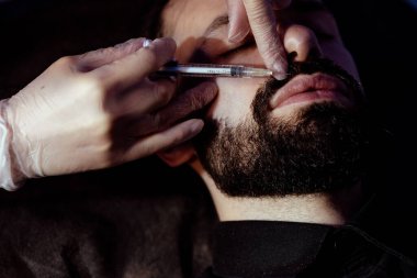 Güzellik uzmanında çeşitli güzellik tedavileri gören rahat genç bir adam sakallı bir adamın portresi güzellik iğneleri ve yüz maskeleri olan bir adam.