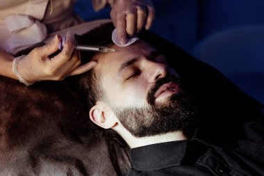 Güzellik uzmanında çeşitli güzellik tedavileri gören rahat genç bir adam sakallı bir adamın portresi güzellik iğneleri ve yüz maskeleri olan bir adam.