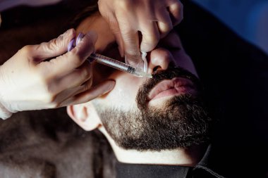 Güzellik uzmanında çeşitli güzellik tedavileri gören rahat genç bir adam sakallı bir adamın portresi güzellik iğneleri ve yüz maskeleri olan bir adam.