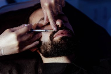 Güzellik uzmanında çeşitli güzellik tedavileri gören rahat genç bir adam sakallı bir adamın portresi güzellik iğneleri ve yüz maskeleri olan bir adam.