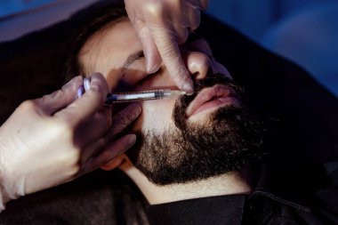 Güzellik uzmanında çeşitli güzellik tedavileri gören rahat genç bir adam sakallı bir adamın portresi güzellik iğneleri ve yüz maskeleri olan bir adam.