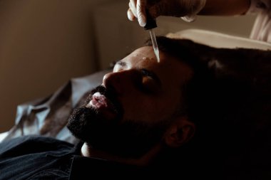 Güzellik uzmanında çeşitli güzellik tedavileri gören rahat genç bir adam sakallı bir adamın portresi güzellik iğneleri ve yüz maskeleri olan bir adam.