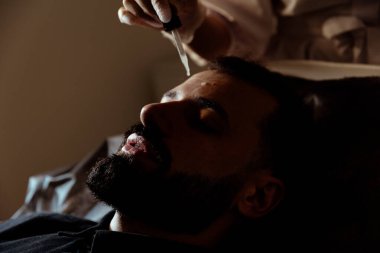 Güzellik uzmanında çeşitli güzellik tedavileri gören rahat genç bir adam sakallı bir adamın portresi güzellik iğneleri ve yüz maskeleri olan bir adam.