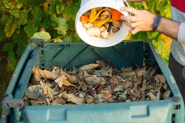 stock image A young man is emptying a bucket with organic waste in a outdoor compost bin.The compost bin is placed in a home garden to recycle organic waste produced in home and garden and produce organic fertilizer. Concept of recycling and sustainability