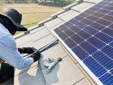 Bir teknisyen çatıya güneş enerjisini binaya güç sağlamak için güneş panelleri kuruyor..