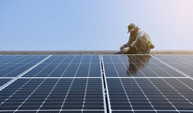 Bir teknisyen çatıya güneş enerjisini binaya güç sağlamak için güneş panelleri kuruyor..