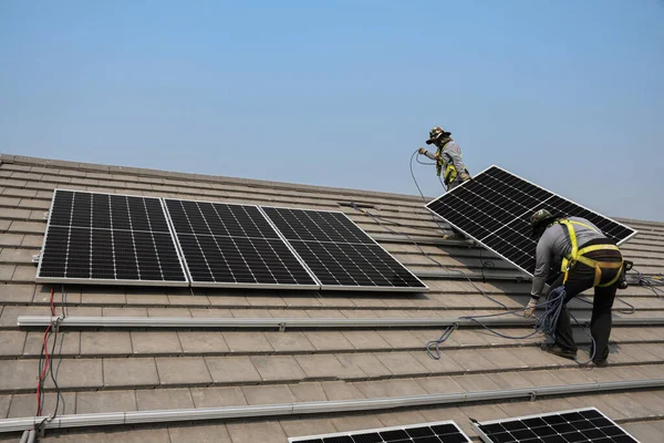 technicians are installing solar panels on the roof to use solar energy to power the building.