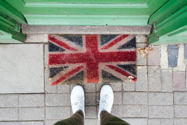 Welcome to the UK. A First-Person View of Legs on a Welcome Mat