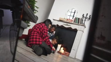 Noel arifesi. Genç bir aile şöminenin yanında bebekle oynuyor. Yüksek kalite 4k görüntü