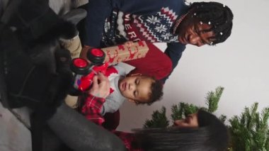 Dikey - Genç çok ırklı aile Noel ağacının yanında bebekle oynuyorlar hediye paketleriyle. Yüksek kalite 4k görüntü