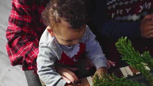 赤ちゃん おもちゃの車とクリスマスツリーの近くで楽しんでいる若い多人種家族 幸せな家族の概念 高品質4K映像 — ストック動画