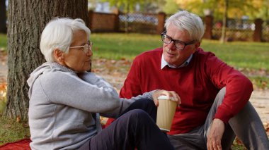 Senior man and woman talking while sitting on the grass in the park. High quality photo