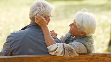 Back view of grey-haired senior couple sitting close together on a bench. High quality photo