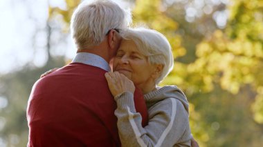 Retired grey-haired woman hugging her husband outdoor. High quality photo