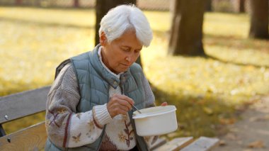 Senior grey-haired woman eating donated charity meal outdoor. High quality photo