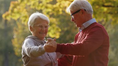 Smiling healthy old couple dancing in the park on a sunny day. High quality photo