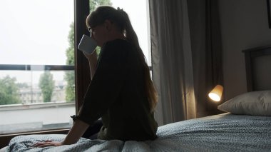 back view of a woman on a bed drinking hot coffee and relaxing, cozy mood. High quality photo