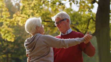 Happy mature grey-haired couple dancing in the park. High quality photo