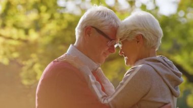 Senior grey-haired couple laughing and hugging with foreheads pressed together. High quality 4k footage