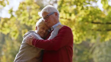 Two loving grey-haired people hugging outdoor in autumn nature. High quality photo