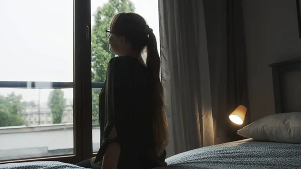 cozy morning, woman with long hair sitting on a bed and looking outside. High quality photo